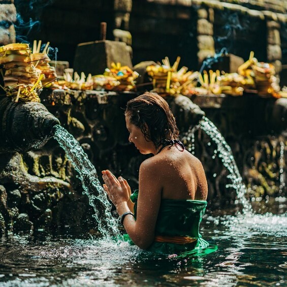 Una persona con un abito verde che prega accanto a una fontana con offerte. 1