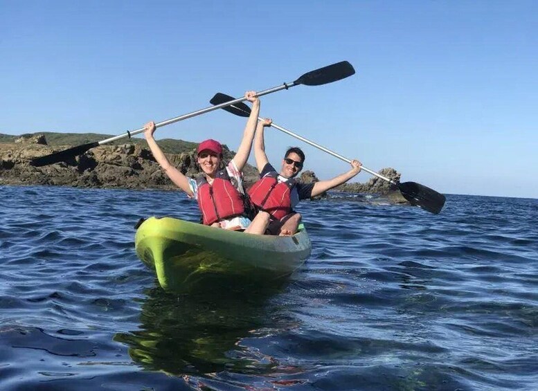 Two people kayaking on a calm sea with rocky cliffs in the background. 3