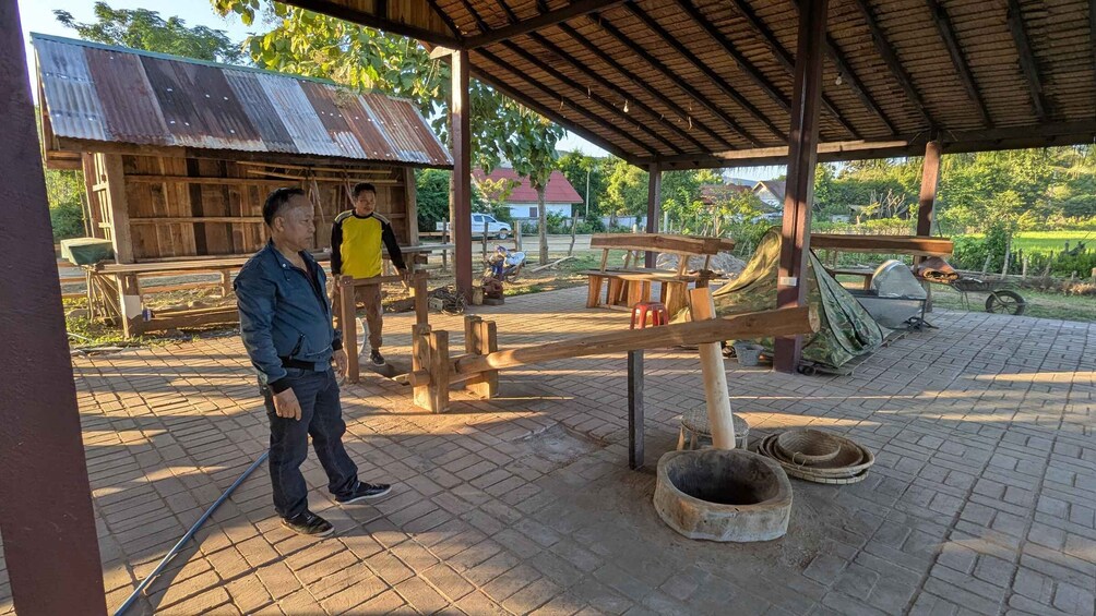 A rustic outdoor setting with a wooden structure, a bench, and a traditional grinding stone. 4