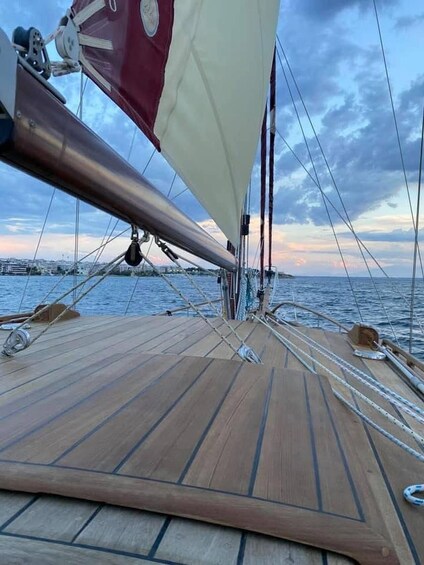 A wooden deck of a sailboat with a red and white sail, ropes, and a cloudy sky. 2