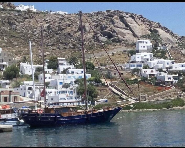A traditional sailing boat docked near a coastal village with white buildings and rocky hills in the background. 4