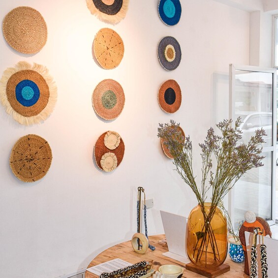 A wall with various woven art pieces, a vase with flowers, and a laptop on a wooden table. 2