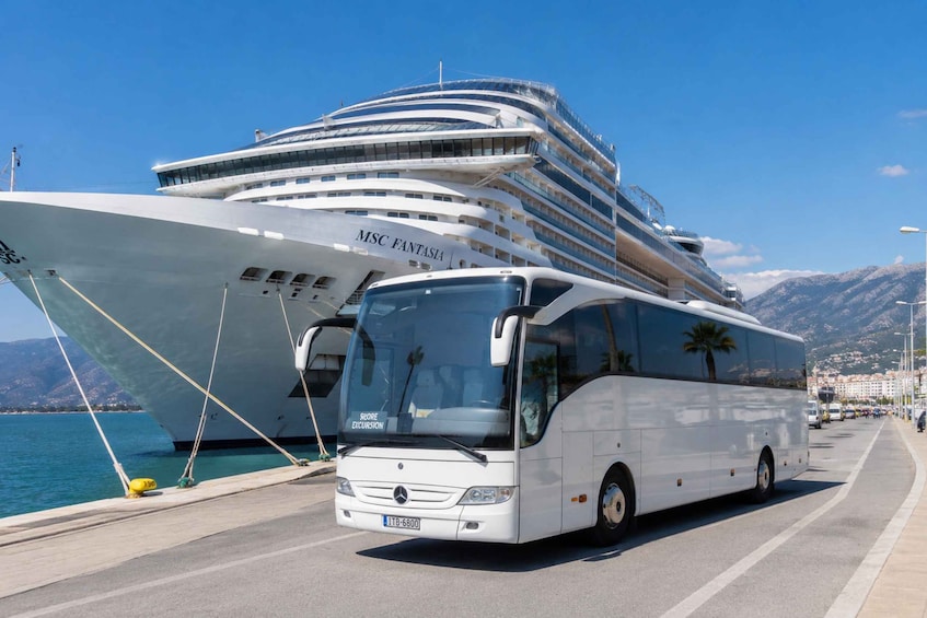 A white cruise ship named MSC Fantasia docked at a port, with a white bus in front. 1