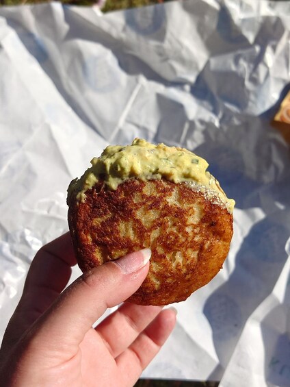 A hand holding a food item with a golden-brown crust, possibly a fritter or pastry, with a creamy topping. 1