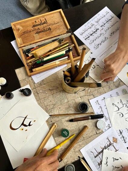 A person writing calligraphy with various tools and papers on a table. 1
