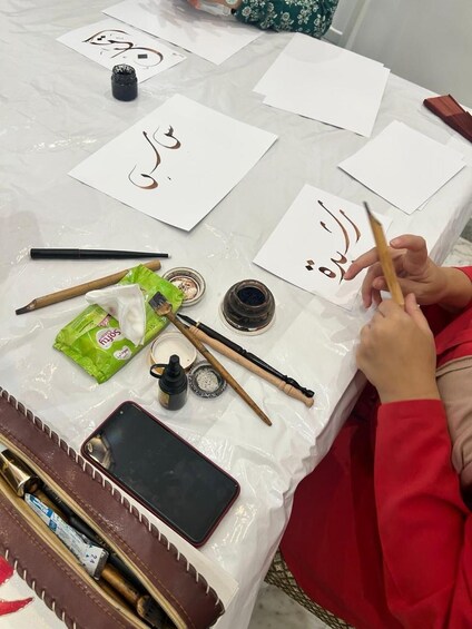 A person practicing calligraphy with ink bottles, brushes, and paper on a table. 5
