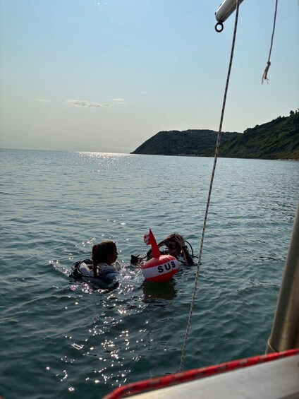 Two people in the water with a red and white buoy marked 'SUB' between them. 2