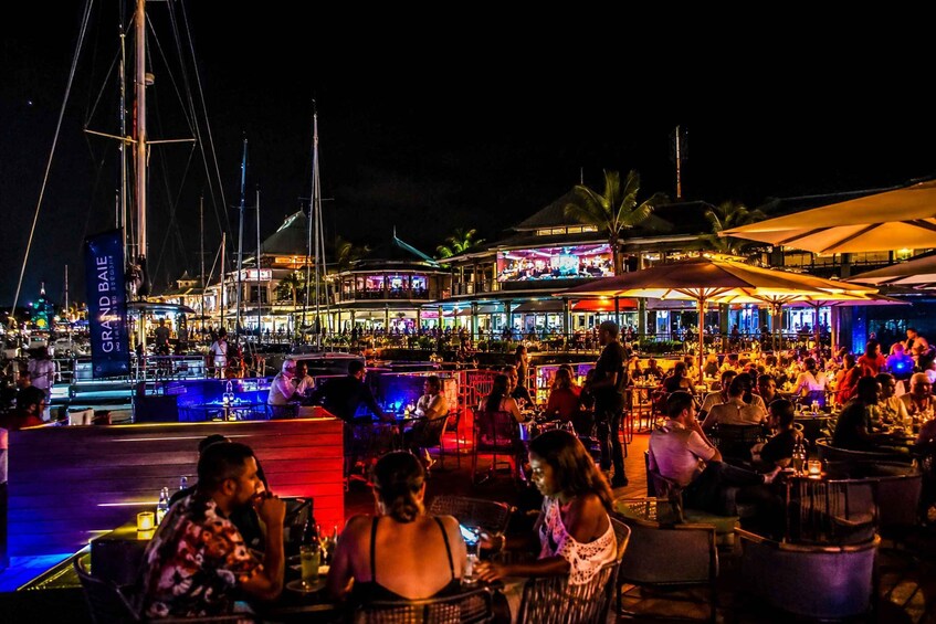 A lively waterfront bar with patrons seated at tables, illuminated by ambient lighting. 1