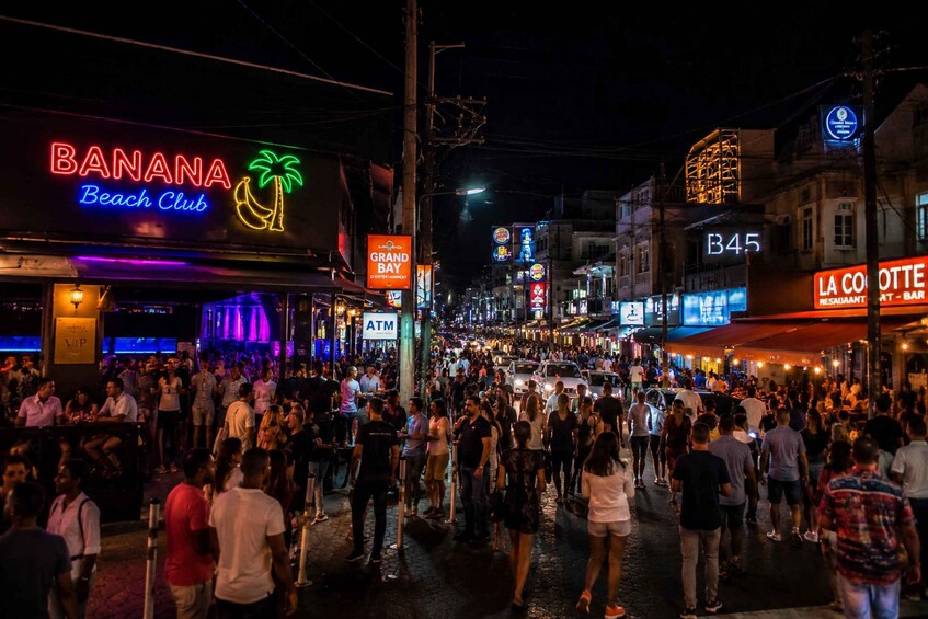 A crowded street at night with neon signs, including 'BANANA Beach Club' and 'B45.' 3