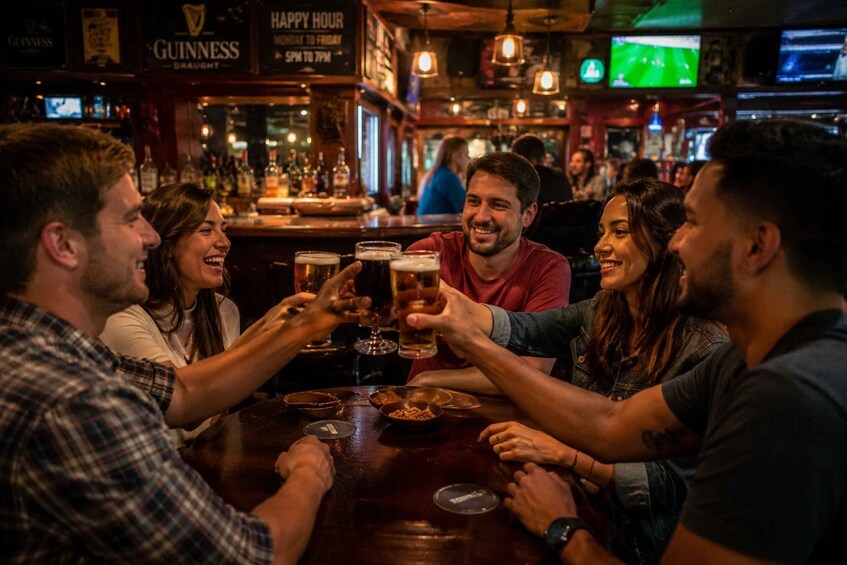 A group of people toasting with beer at a bar with Guinness signage. 4