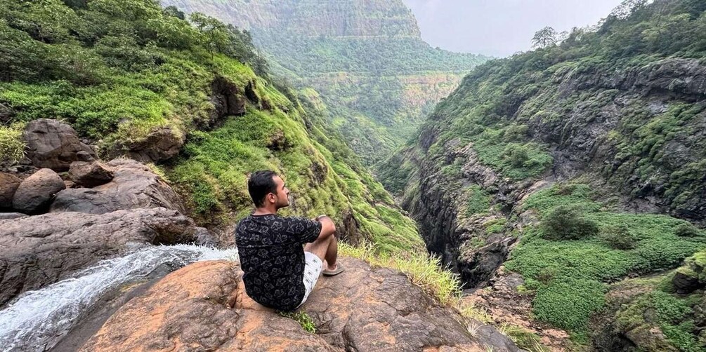 A person sitting on a rock by a waterfall in a lush valley. 3