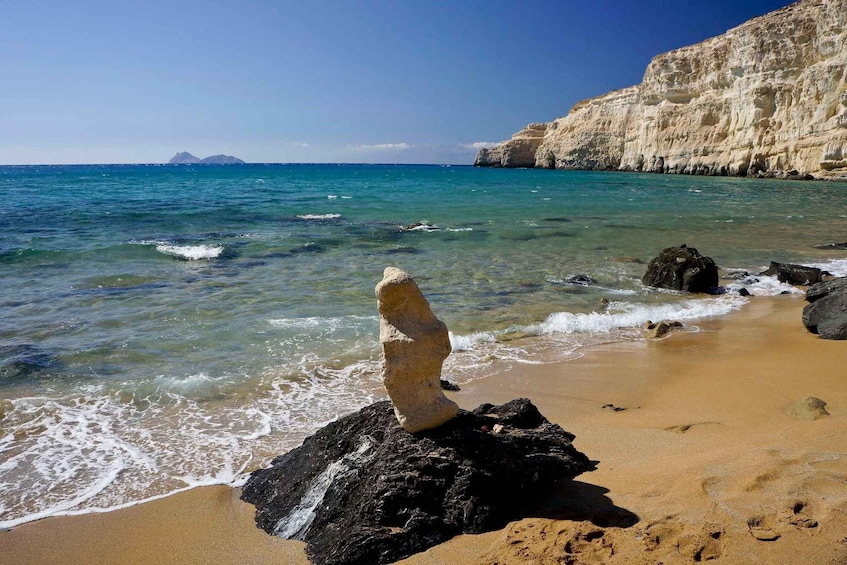 A coastal landscape with clear blue waters, a sandy beach, rocky formations, and distant cliffs. 3