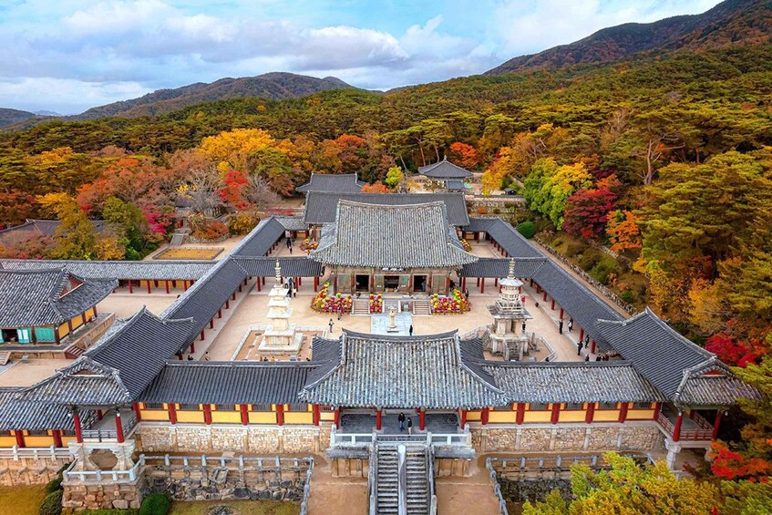 A traditional Korean temple complex with tiled roofs and stone walls, surrounded by autumn-colored trees. 3