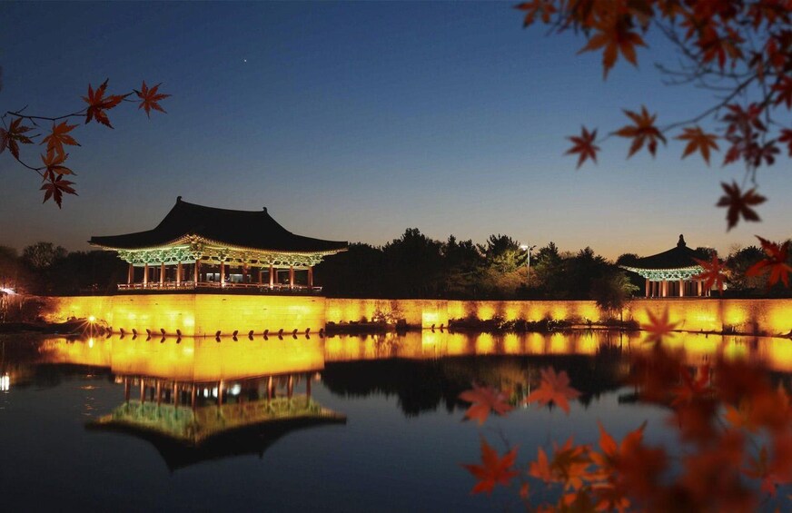 A traditional building with a tiled roof, reflecting in a calm body of water, surrounded by autumn foliage. 5