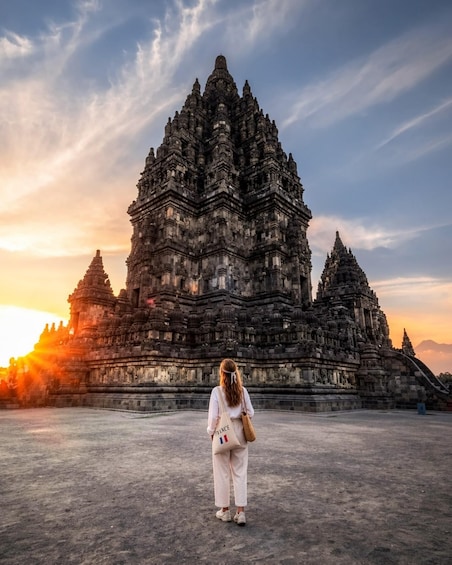 A person standing in front of a large, intricately designed temple with multiple spires, during sunset. 1