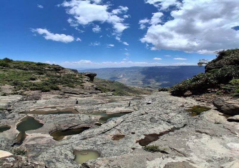 Paesaggio roccioso con pozze d'acqua e una vista lontana delle montagne sotto un cielo parzialmente nuvoloso. 3