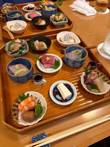 A wooden tray with various Japanese dishes, including sashimi, sushi, and pickled vegetables. 3