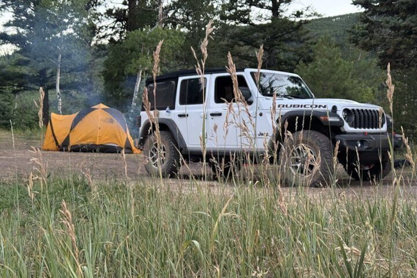 A white Jeep Rubicon parked in a grassy field with a yellow tent in the background. 2