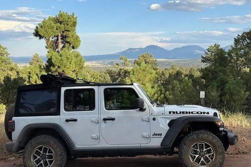 A white Jeep Rubicon parked on a dirt road with a mountainous landscape in the background. 3