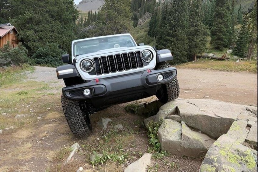 A white off-road vehicle parked on a dirt path surrounded by rocks and greenery. 1