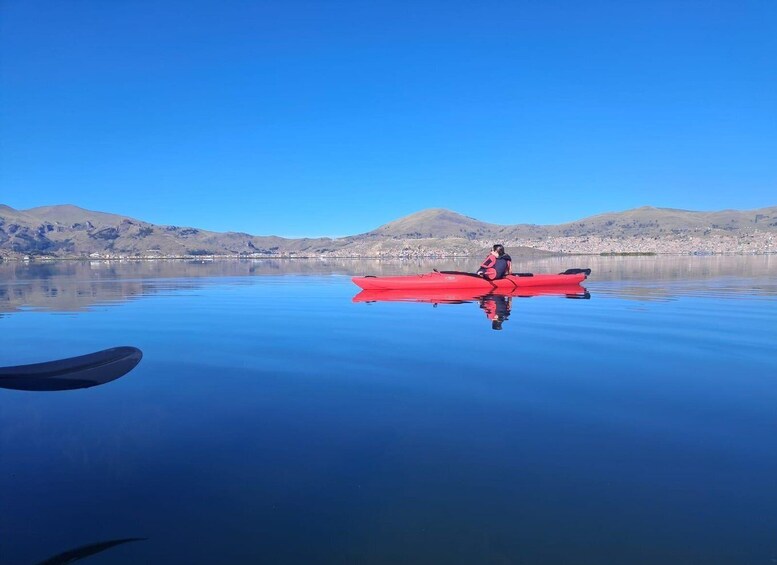 A person in a red kayak on calm water with mountains in the background. 3