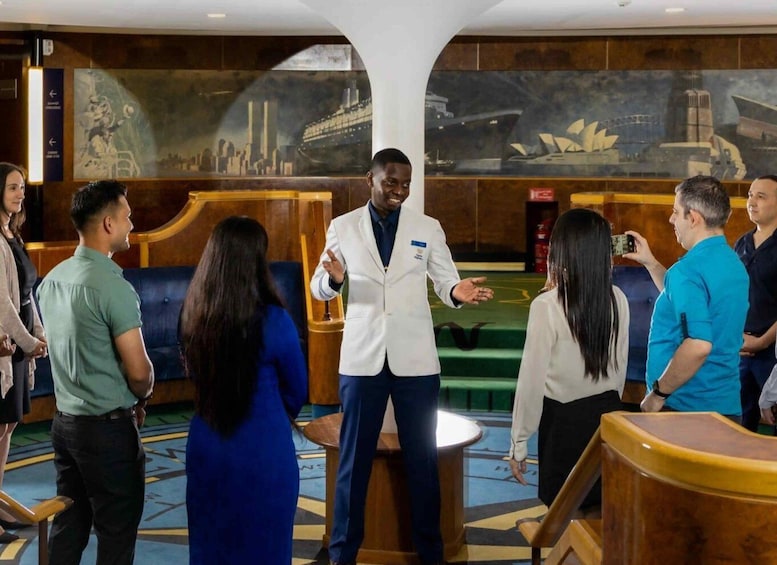 A man in a white coat speaking to a group of people in a room with nautical-themed murals. 5