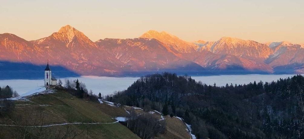 A church on a hill overlooking a lake with mountains in the background. 1