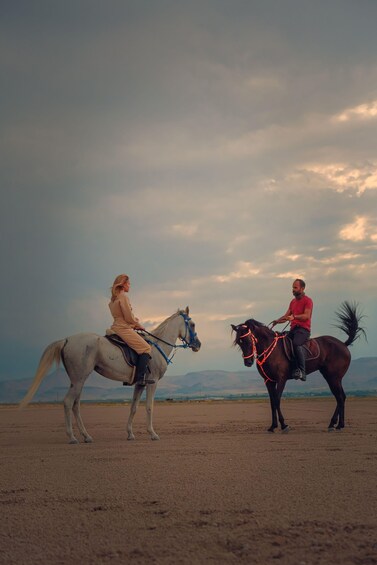 Two people on horses in an open field with a cloudy sky. 3