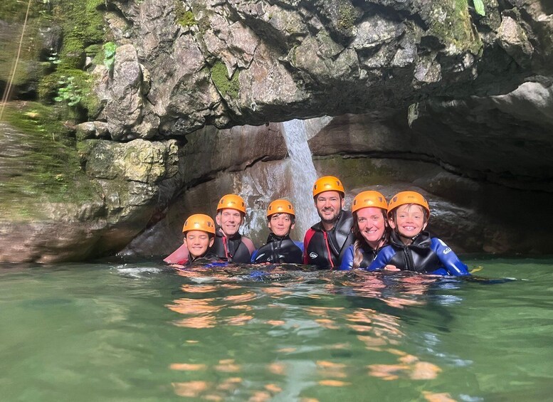 A group of people in water with helmets, a waterfall, and rocky terrain. 2