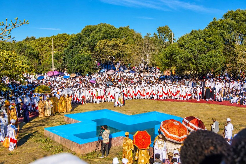 A large outdoor gathering with people in traditional attire, a blue stage, and a crowd watching. 1