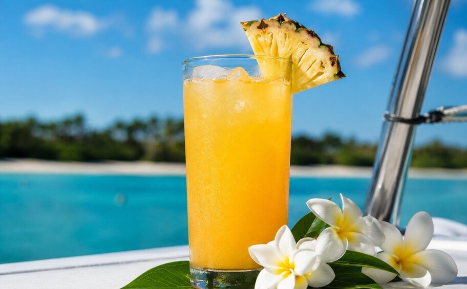 A tall glass of orange juice with a pineapple slice, white flowers, and a pool in the background. 3