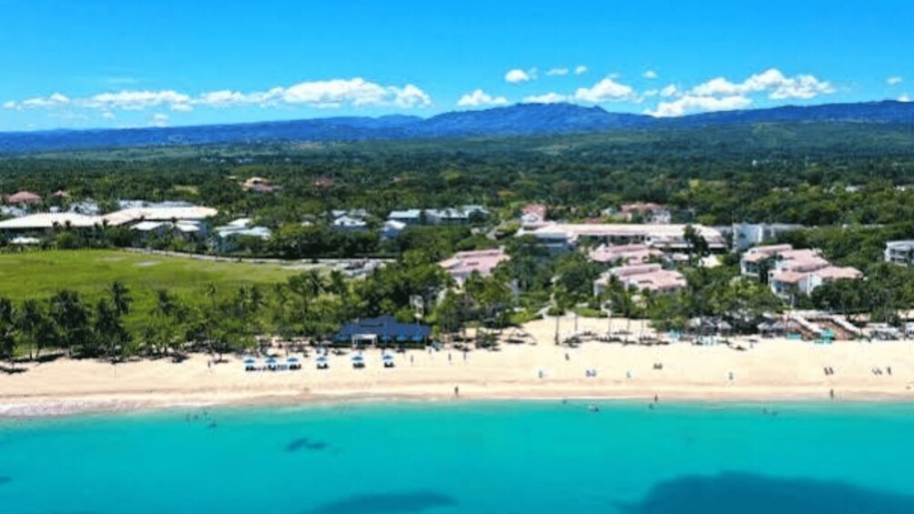 A coastal town with a beach, clear turquoise waters, and a mountainous backdrop. 2