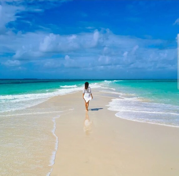 A woman walking on a beach with clear blue water and a bright sky. 2