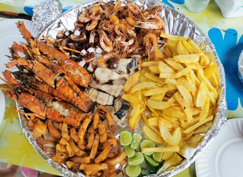 A variety of seafood including grilled shrimp, crab legs, and fish, along with French fries and lime slices on a foil tray. 3