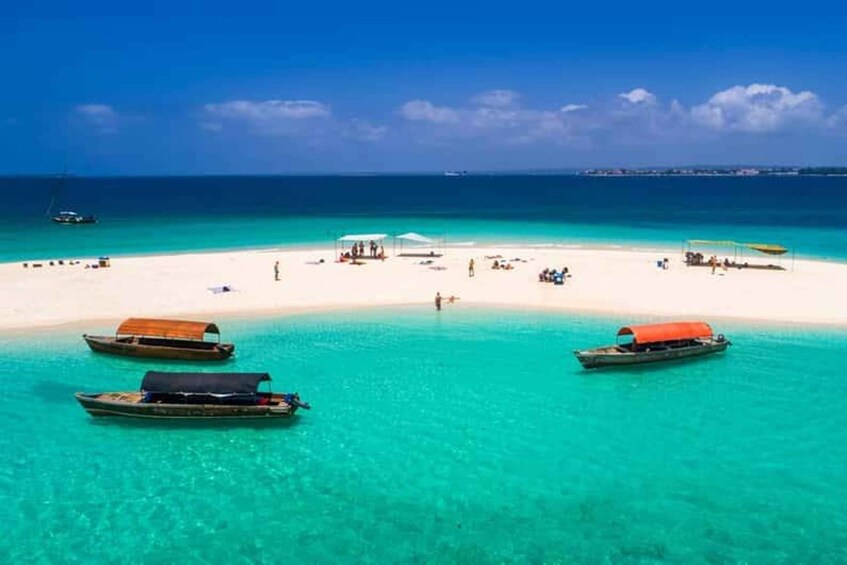 A tropical beach with clear turquoise water, several boats anchored near the shore, and a few people enjoying the beach. 3