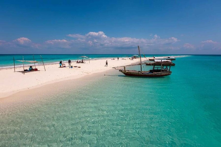 A beach with clear turquoise water, a sandy shore, and a traditional boat anchored nearby. 4
