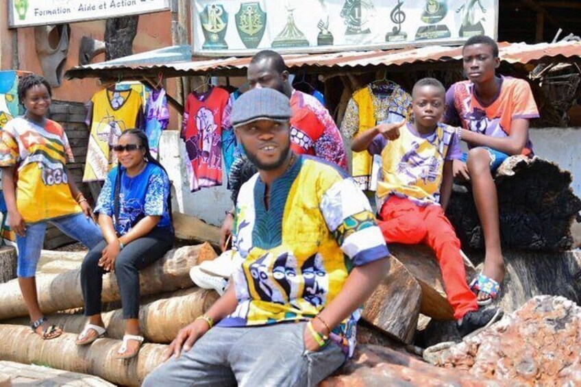 People sitting on logs, wearing colorful clothing, with a sign reading 'Formation Aide et Action' in the background. 3