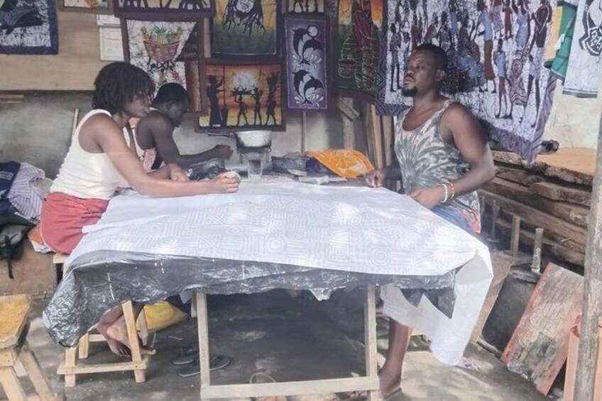 A workshop with a table covered in a patterned cloth, surrounded by wooden planks and art supplies. 4