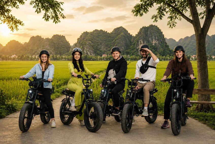 Five people on electric bikes in a rural setting with green fields and mountains in the background. 5