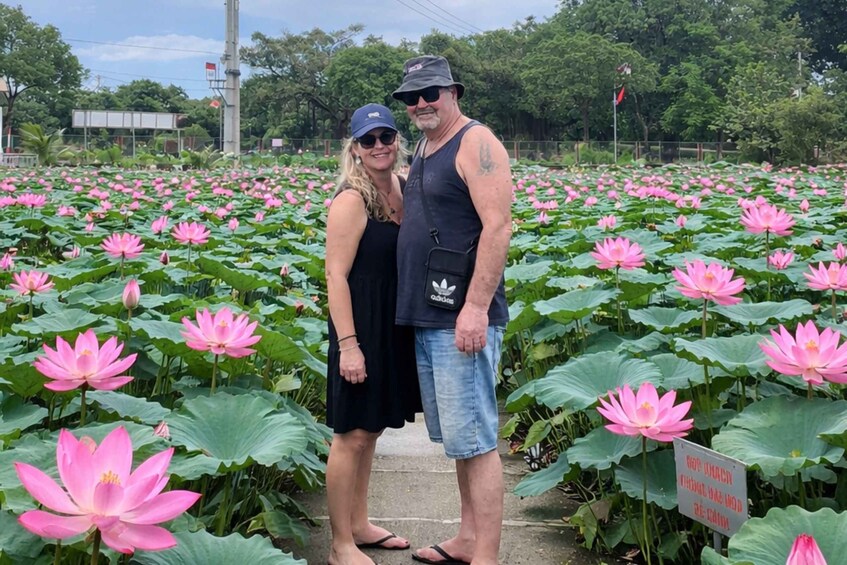 A couple standing among pink lotus flowers in a garden. 2