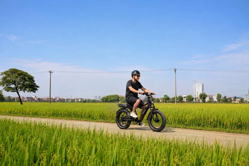 A person riding a black electric scooter on a rural road with green fields and a clear sky. 4