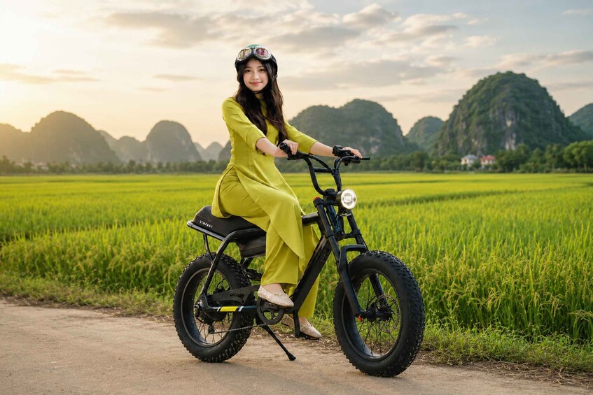A person riding a black electric bike on a dirt path through a green field with mountains in the background. 1