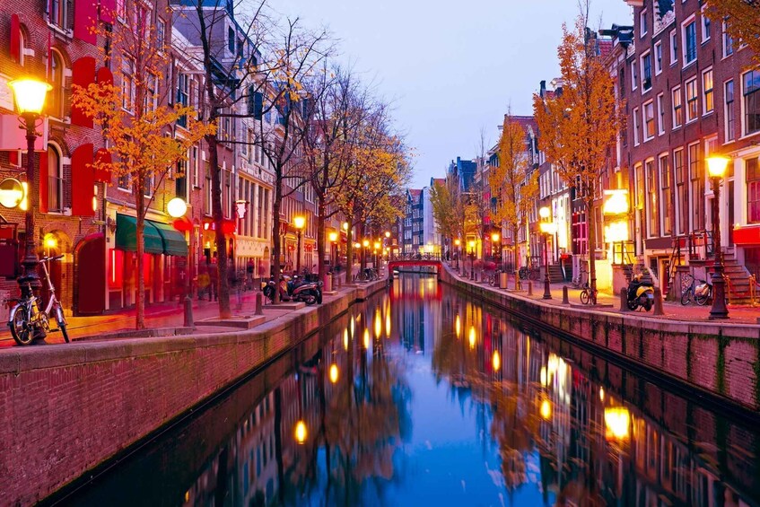 A canal with buildings on either side, bicycles parked along the path, and a red bridge in the distance. 1