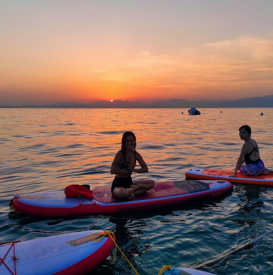 Two individuals sitting on inflatables in calm water during sunset. 2