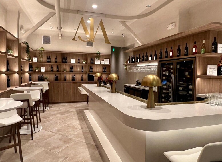 A modern bar with a curved counter, white bar stools, and a variety of bottles and glasses on shelves. 1