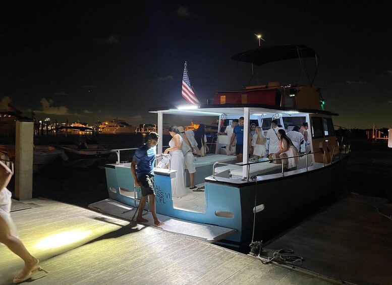 A nighttime scene with a boat docked at a pier, an American flag, and a cityscape in the background. 5