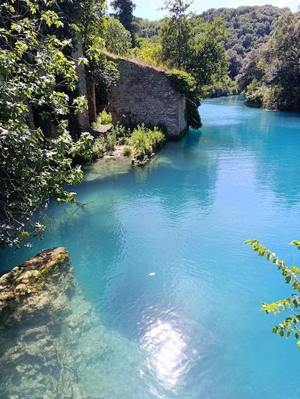 A clear blue river with a stone wall and lush greenery. 1