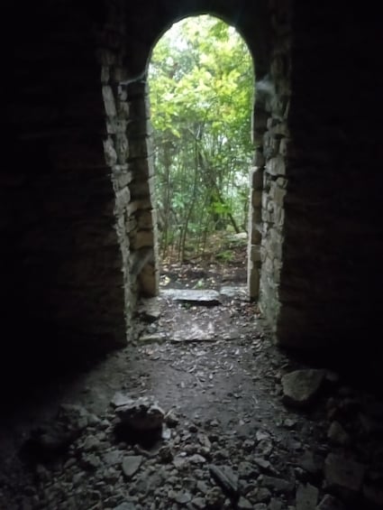 An arched stone structure with a forested path leading through it. 5