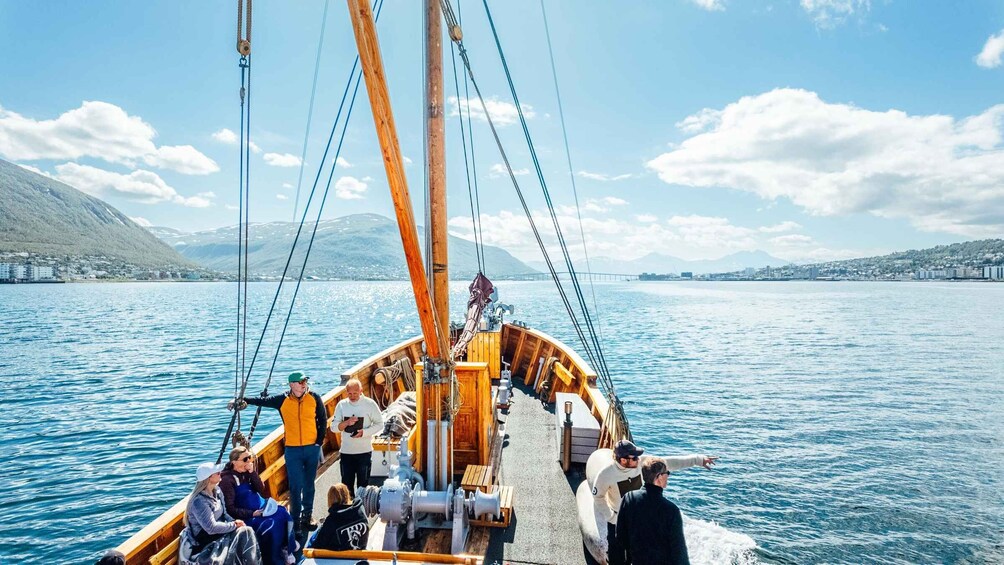 A sailboat with passengers and crew on a calm lake, surrounded by mountains and a distant cityscape. 3