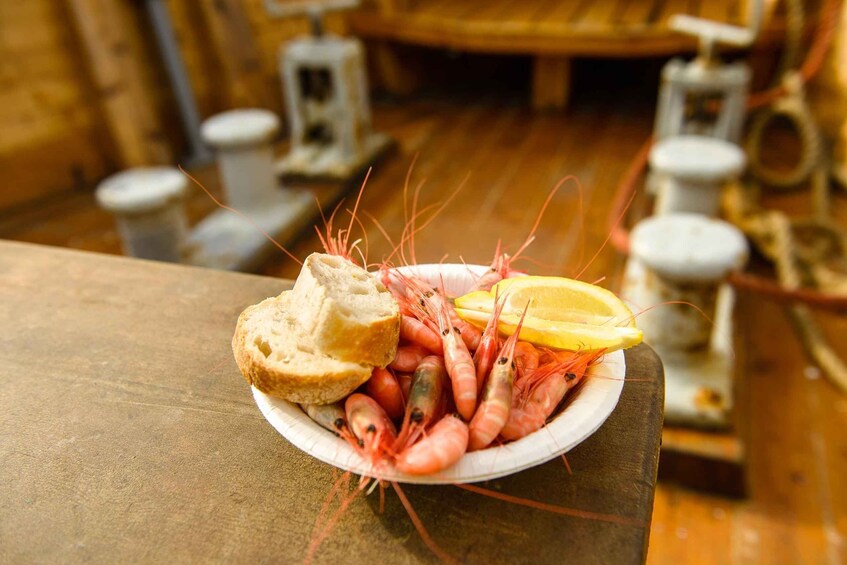 A plate of shrimp, bread, and lemon wedges on a wooden table. 1
